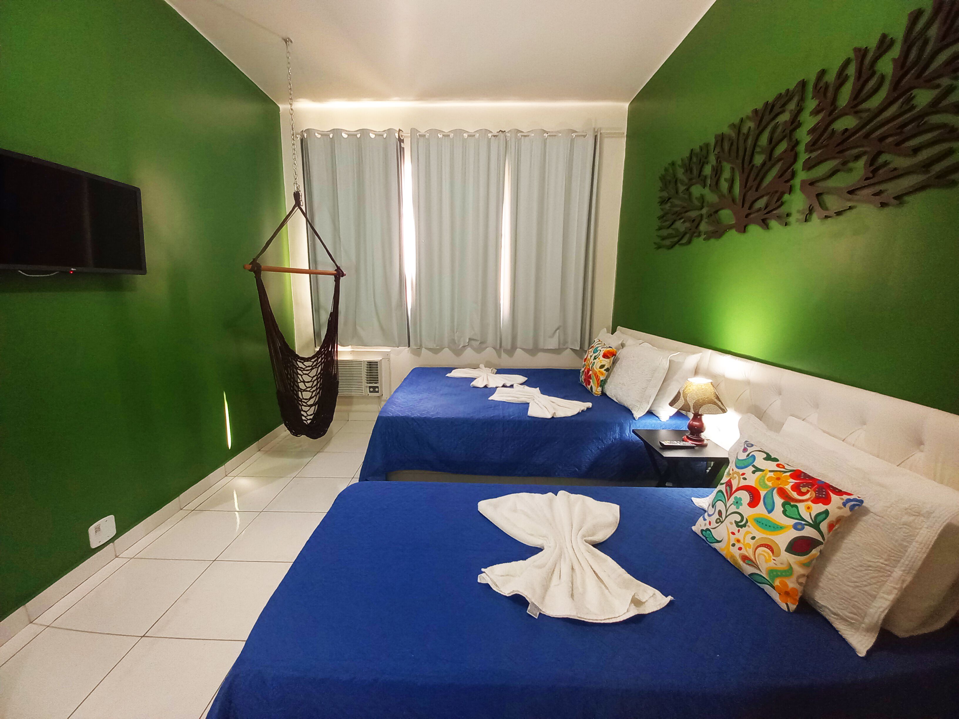 A hotel room with two beds, green walls, a hanging chair, and a flat-screen TV.