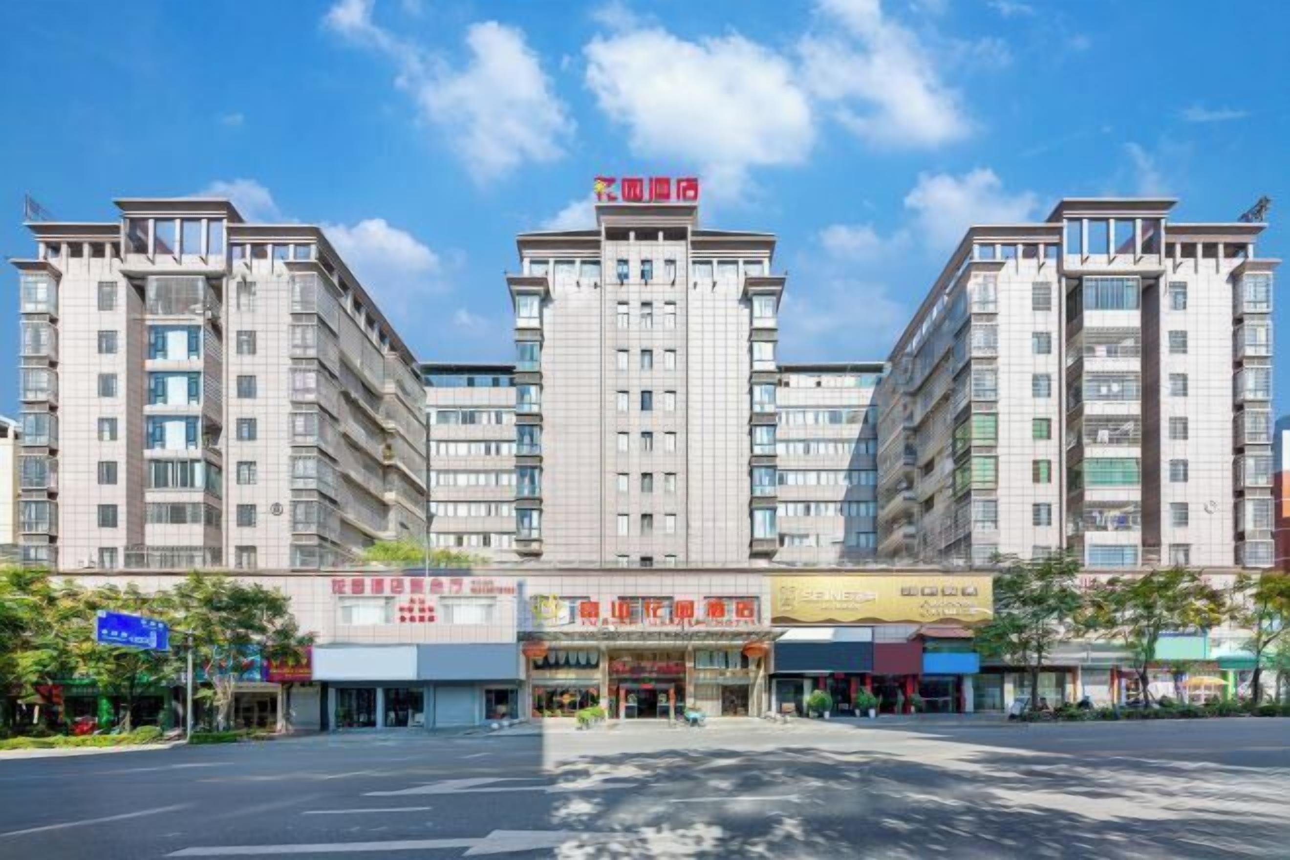 A multi-story hotel with a central entrance, a flag on top, and various shops in front.