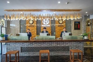 Un comptoir d’accueil avec trois employés, une horloge et une enseigne indiquant « Garden Hotel ».