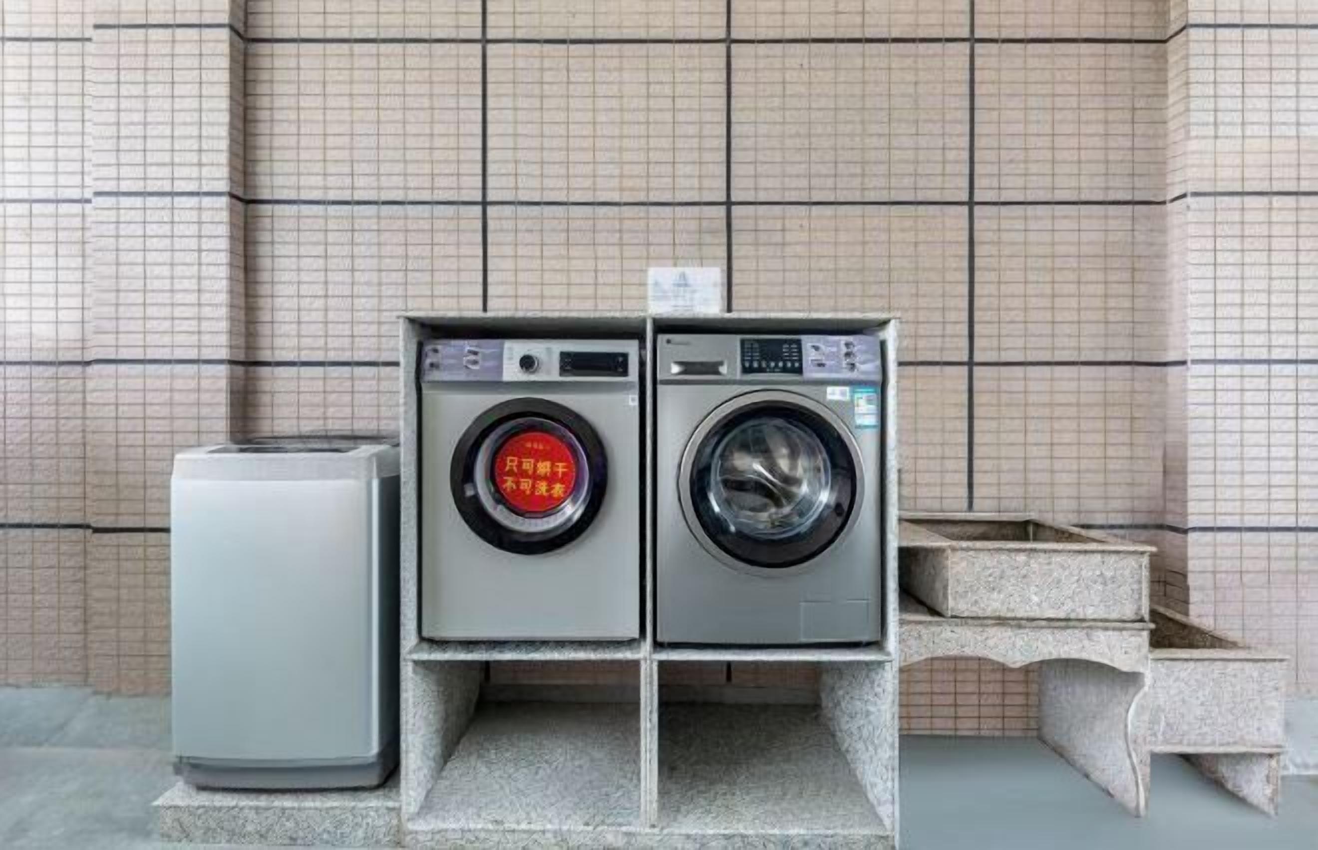 A laundry facility with two washing machines and a dryer, set against a tiled wall.