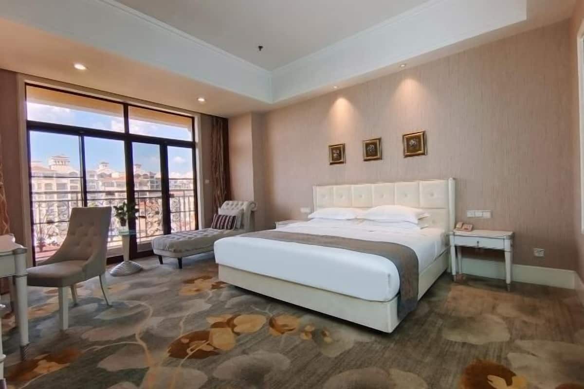 Habitación de hotel con una cama grande, una silla, una mesita y vistas a edificios a través de un ventanal amplio.