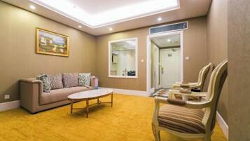 Uma sala de estar com um sofá, cadeiras, uma mesa de centro e um quadro na parede.