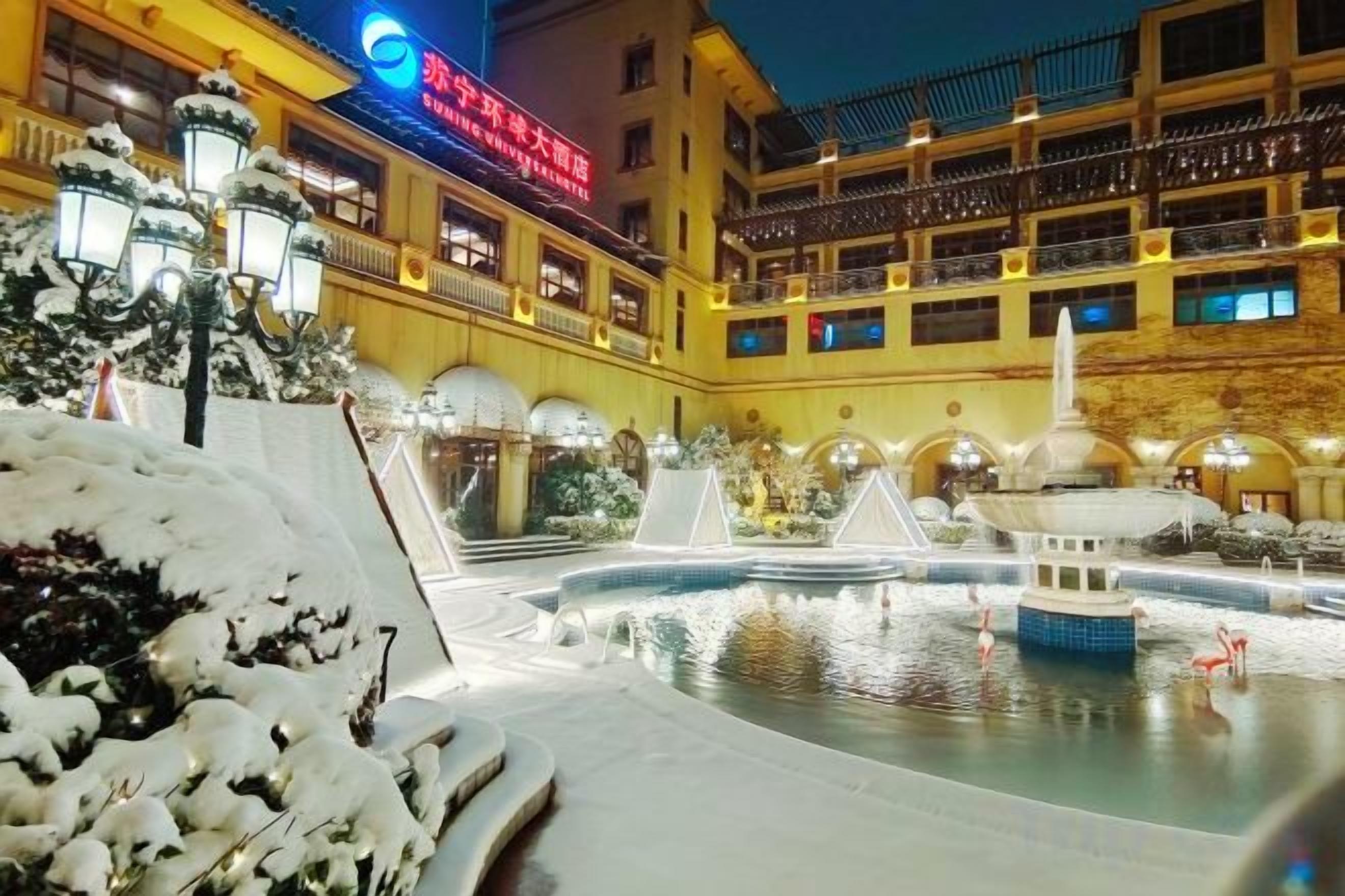A hotel courtyard with a fountain, snow-covered plants, and a building with multiple balconies.