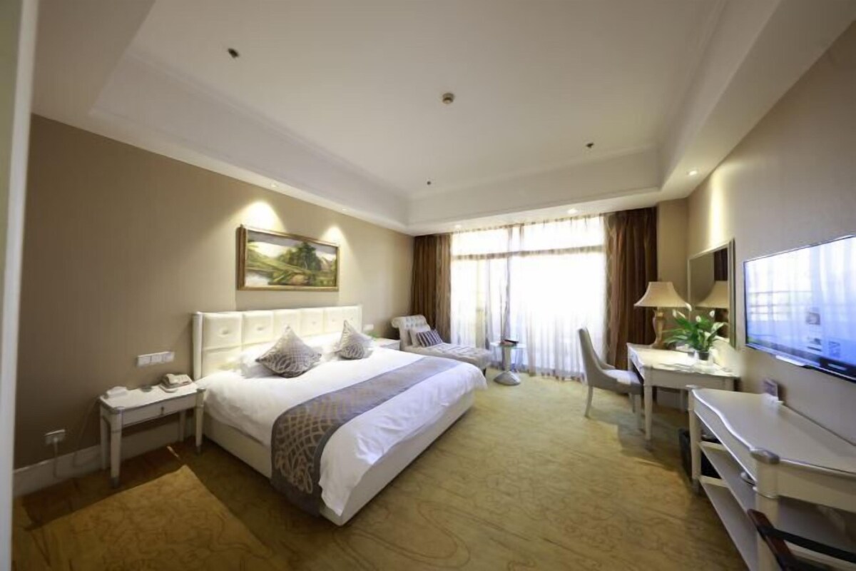 Ein Hotelzimmer mit einem großen Bett, einem Schreibtisch, einem Stuhl, einem Fernseher und einem Gemälde an der Wand.