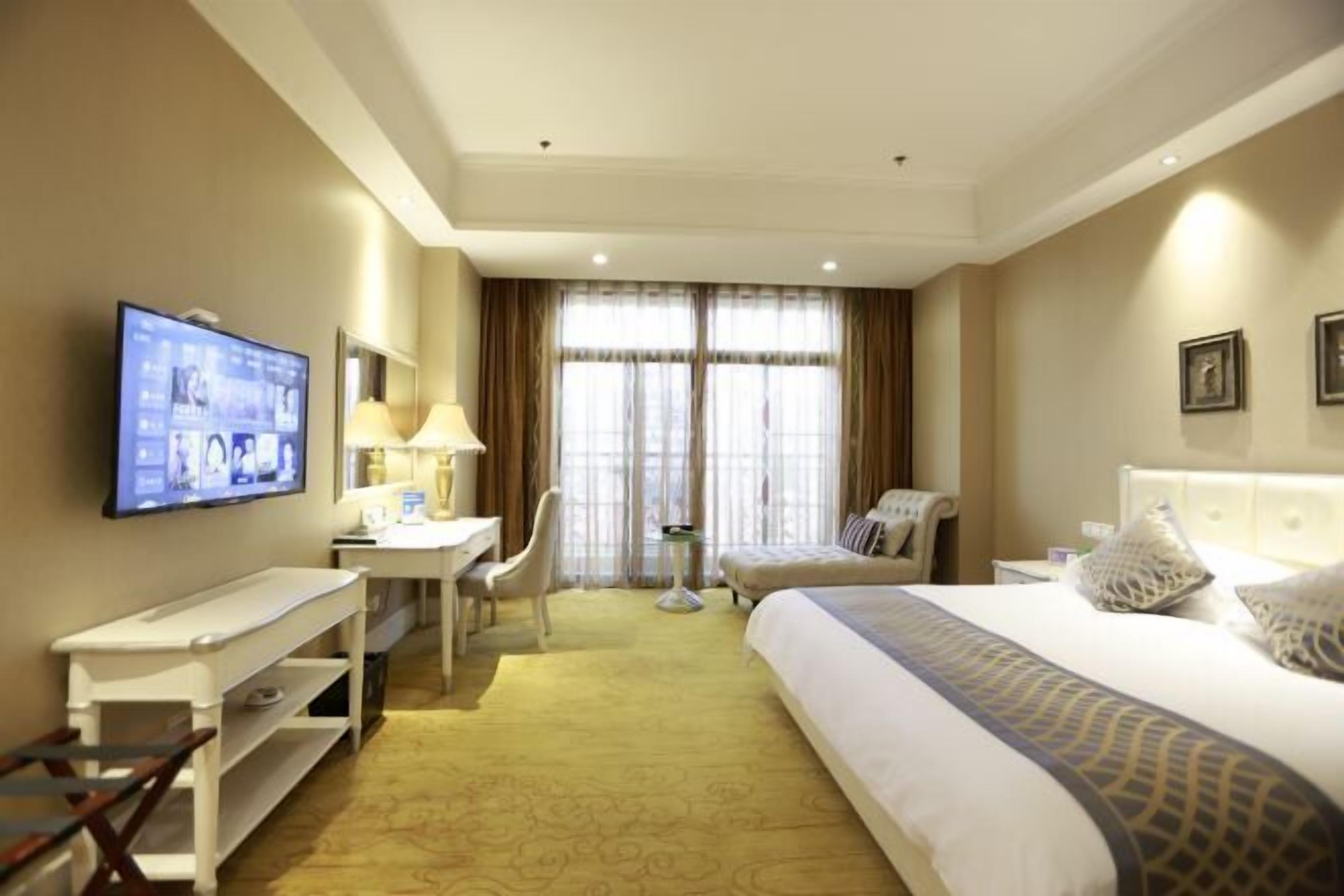 A hotel room with a bed, a desk, a chair, a TV, and a window with curtains.