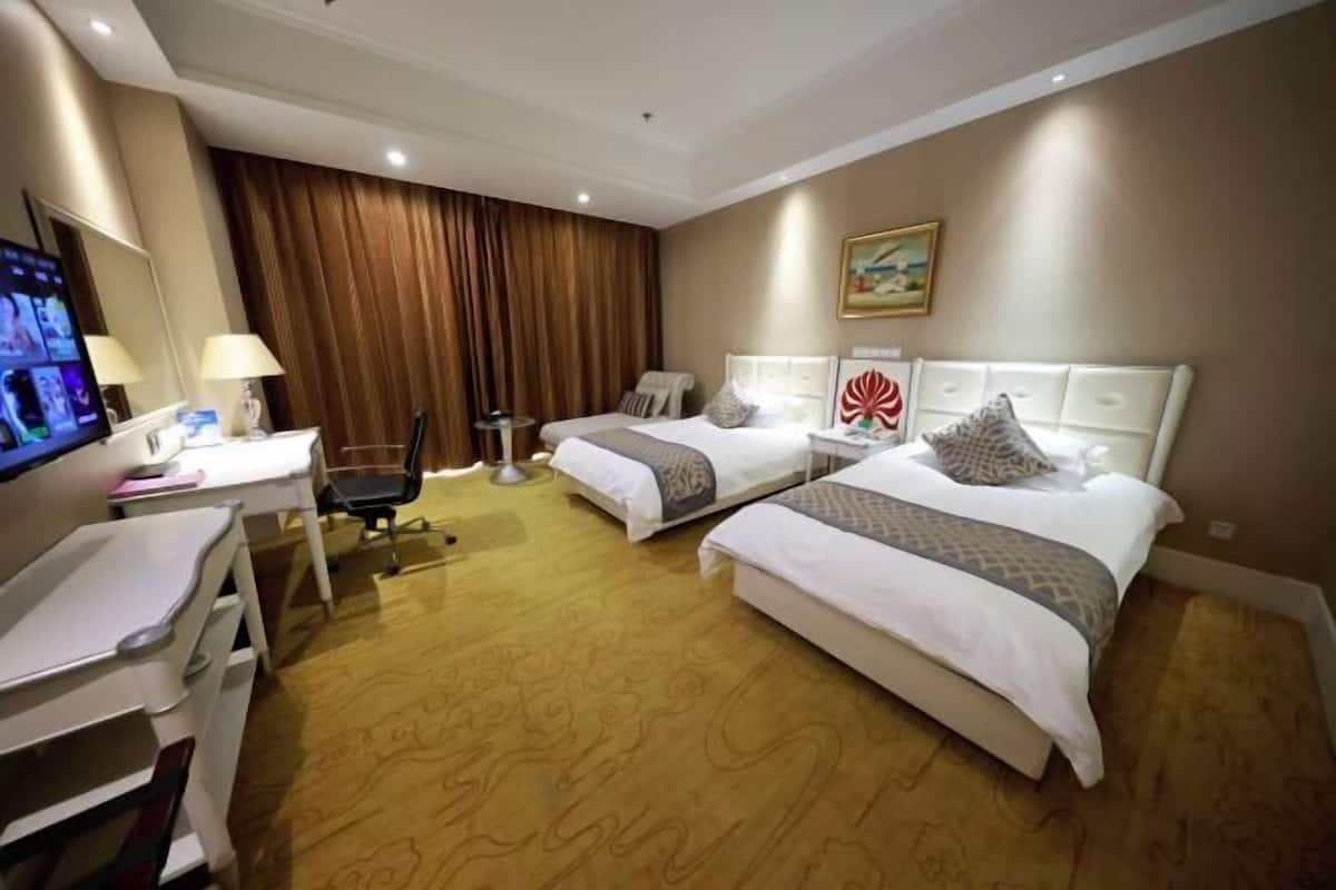 Habitación de hotel con dos camas, un escritorio, una silla, un televisor y un cuadro en la pared.