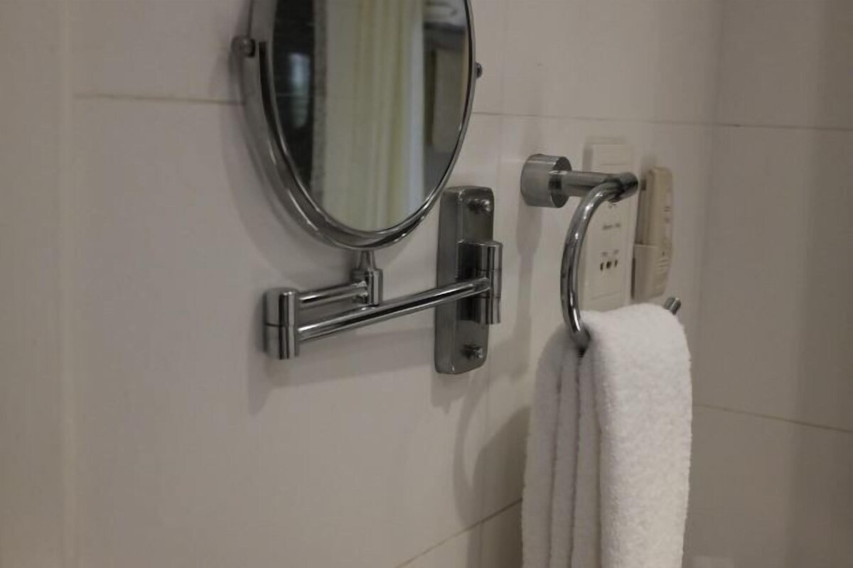 Ein Badezimmer mit Spiegel, Handtuchhalter und einem an der Wand befestigten Steckdosenanschluss.
