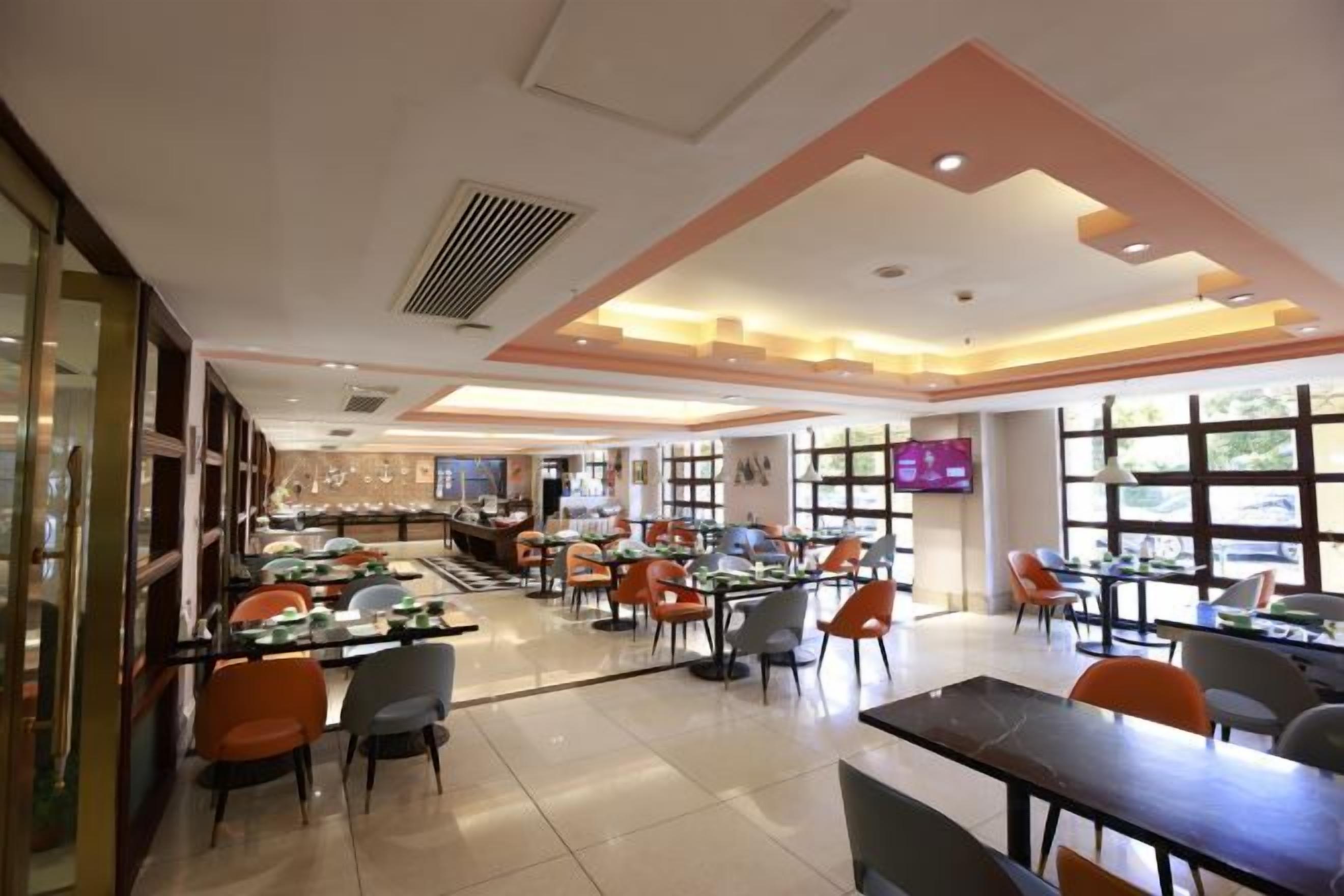 A spacious restaurant with multiple dining tables and chairs, a bar area, and large windows providing natural light.