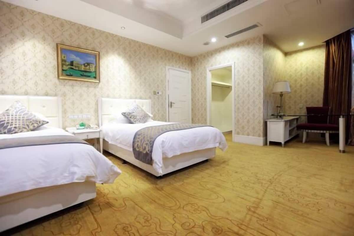 Habitación de hotel con dos camas, un escritorio, una silla, un armario y un cuadro en la pared.