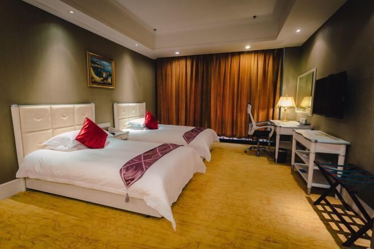 Ein Hotelzimmer mit zwei Betten, einem Schreibtisch, einem Stuhl, einem Fernseher und einem Fenster mit Vorhängen.