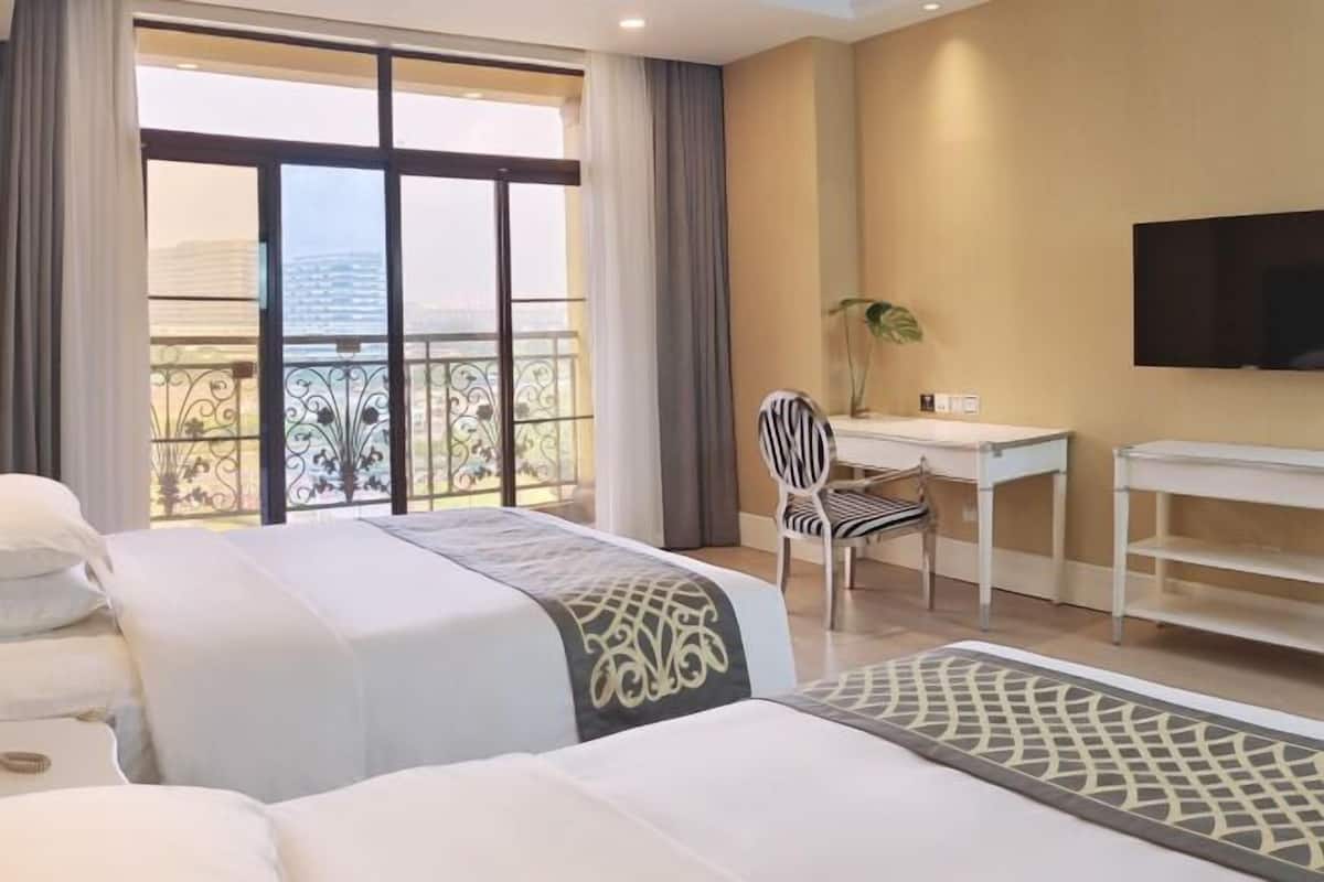 Habitación de hotel con dos camas, un escritorio, una silla, televisión y balcón con vistas.