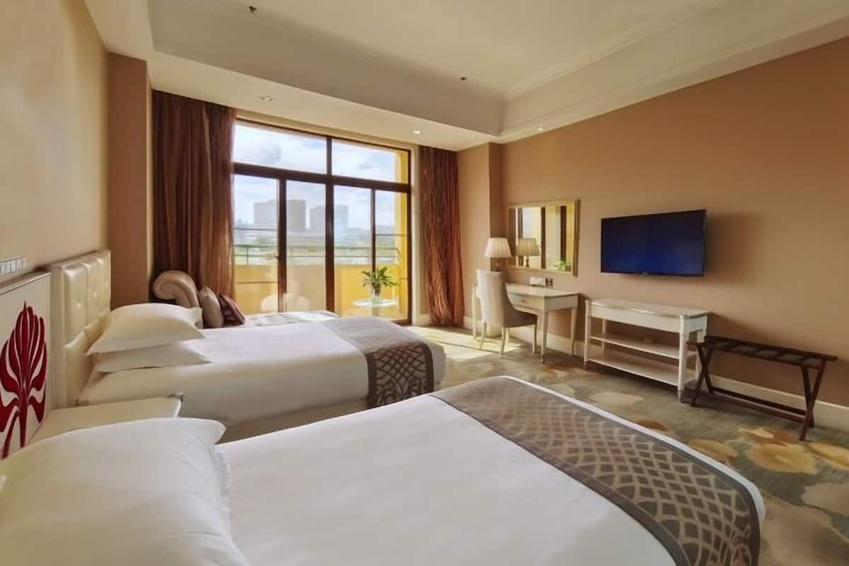 Habitación de hotel con dos camas, un escritorio, televisor y una ventana grande con vistas a la ciudad.