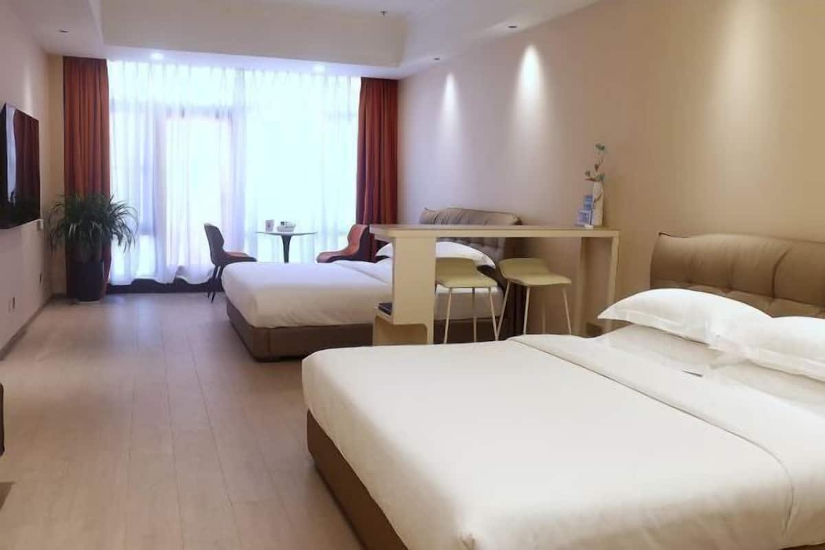 Habitación de hotel con dos camas, un escritorio, una silla, una mesita y una planta en maceta.