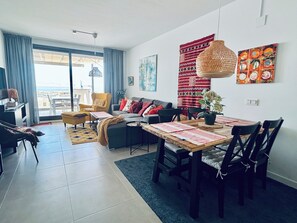 Ein modernes Wohnzimmer mit Sofa, Sesseln, einem Esstisch und Blick durch ein großes Fenster.