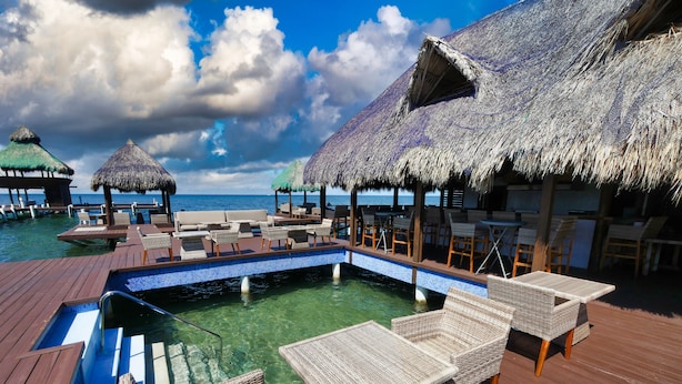 An infinity pool with wicker furniture, thatched umbrellas, and wooden deck.