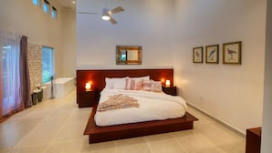 A spacious bedroom with a large bed, a ceiling fan, a nightstand with a lamp, and framed artwork on the wall.