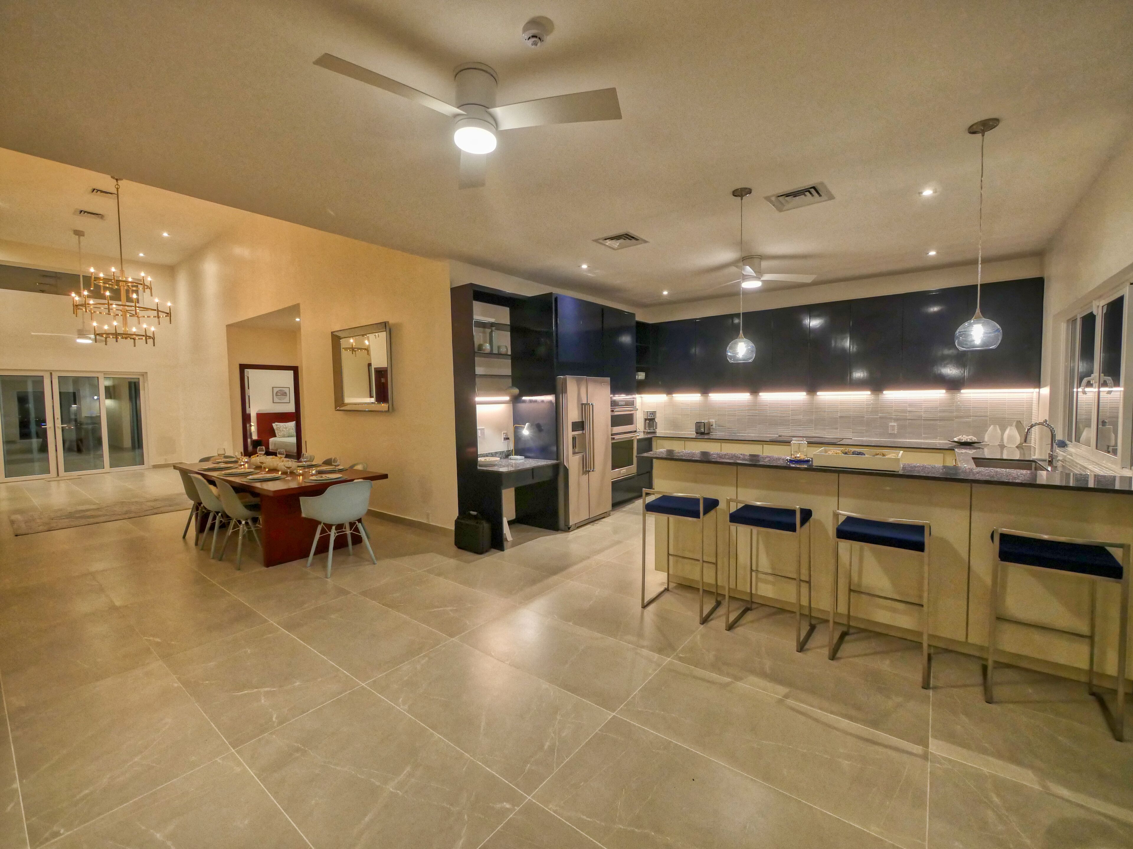 Una cocina moderna con una isla central, taburetes de bar y un comedor con candelabro.