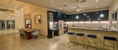 A modern kitchen with a central island, bar stools, and a dining area with a chandelier.