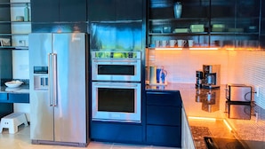 A modern kitchen with a stainless steel refrigerator, double oven, and black cabinets.