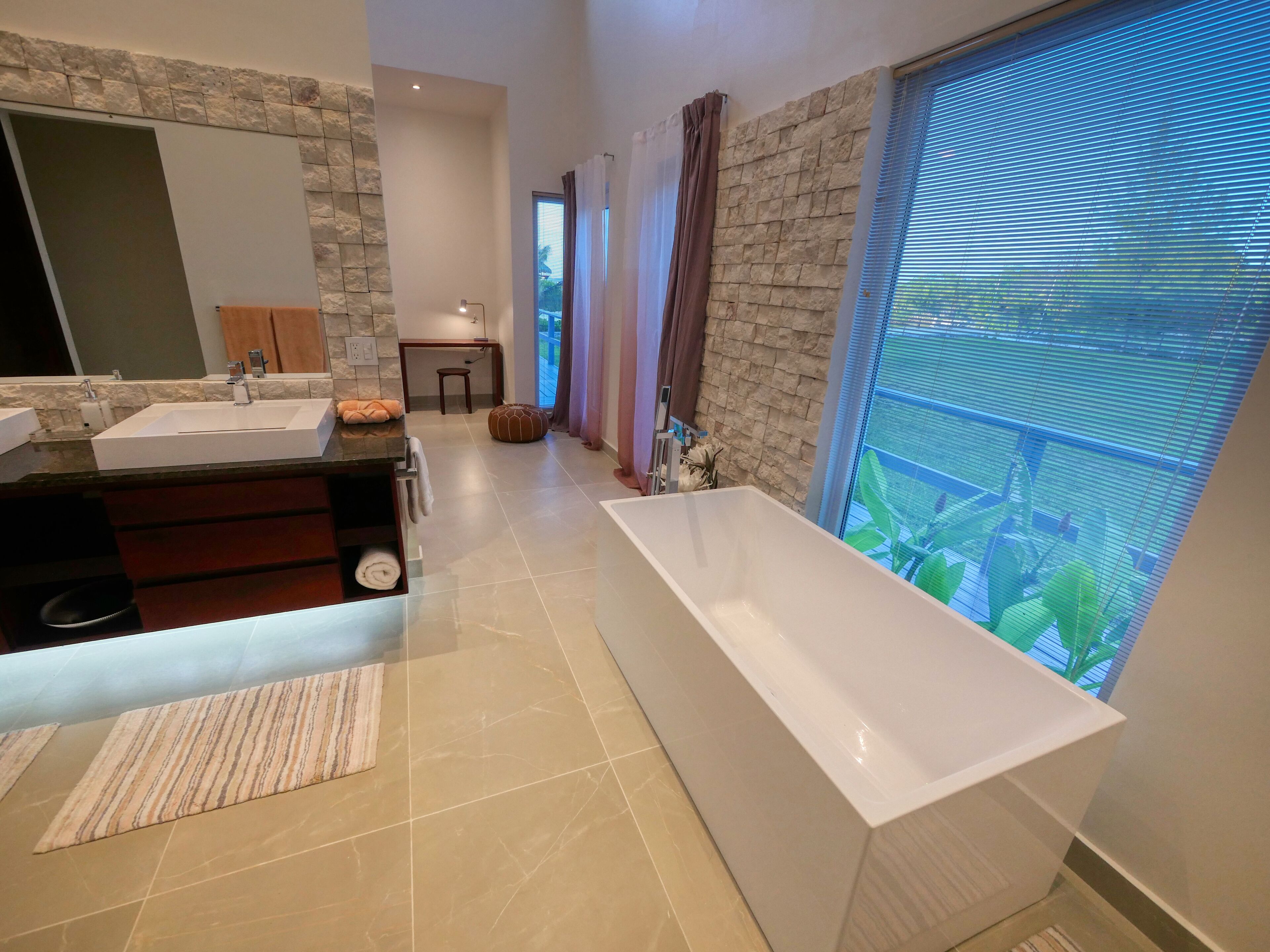 Un bagno moderno con una grande vasca da bagno, un mobile lavabo doppio e una parete decorata con pietra.