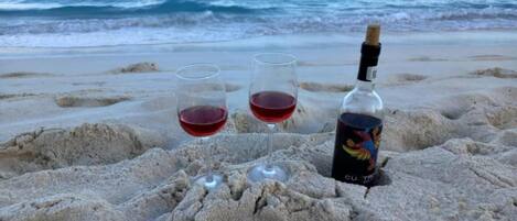 A bottle of wine and two glasses on a sandy beach with the ocean in the background.