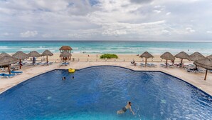 Ein Swimmingpool mit Blick auf den Ozean, umgeben von Liegestühlen und Reetdachschirmen.