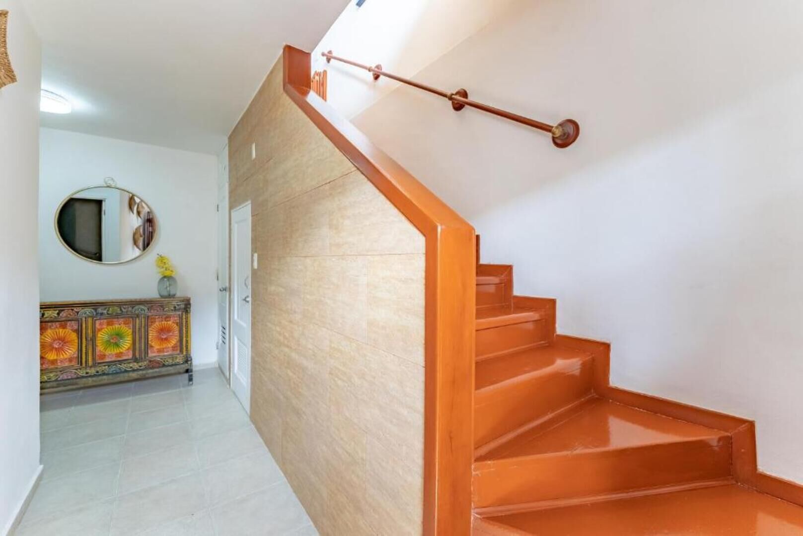 Eine Treppe mit Holzboden und Geländer, die zu einer Tür mit Spiegel und einer Zierkommode führt.