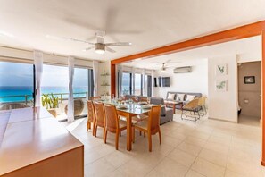 A spacious living area with a dining table, sofas, and a balcony with a view of the ocean.