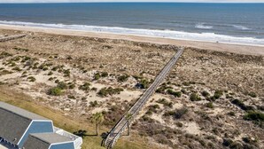 A beach with a long wooden boardwalk leading to the shore, surrounded by sparse vegetation.