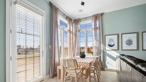 Un comedor con una mesa y sillas, ventanas grandes con persianas y vistas al exterior.