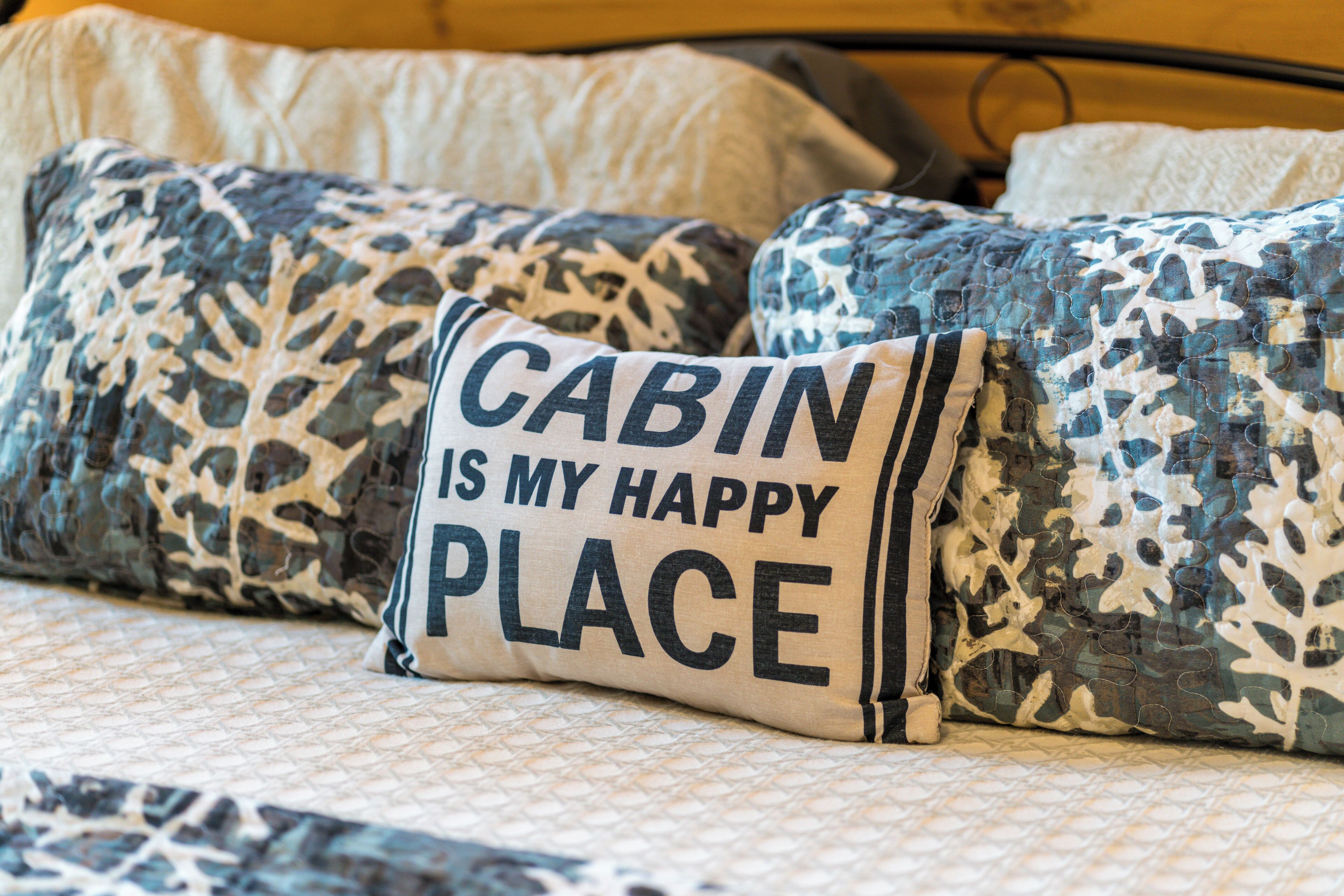 Ein Bett mit gemusterten Kissen und einem Kissen mit dem Aufdruck "CABIN IS MY HAPPY PLACE".