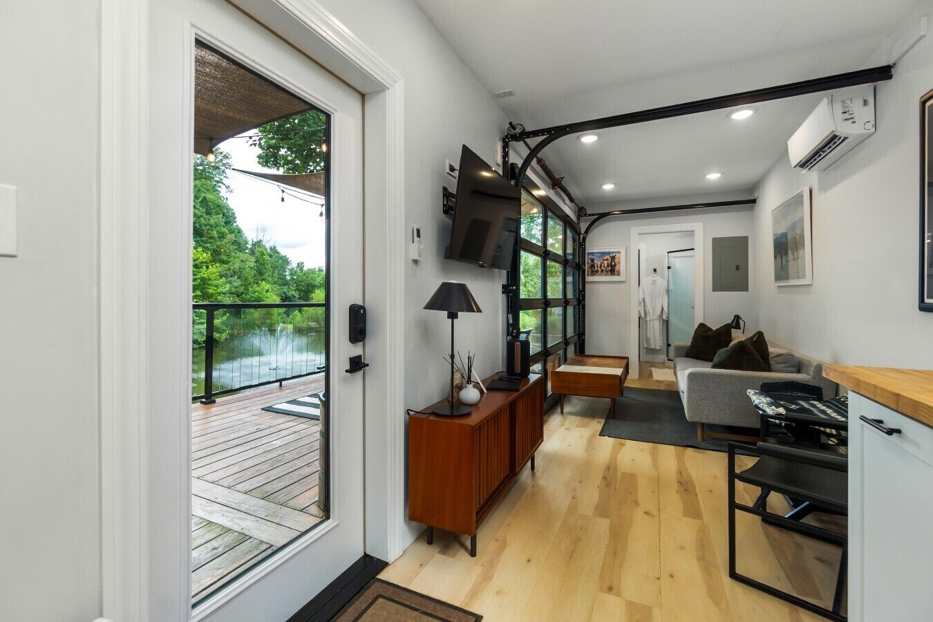 Een modern interieur met een houten vloer, een bank, een televisie en uitzicht op een balkon met een hekwerk.
