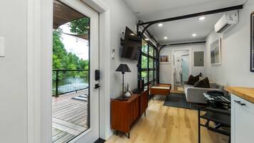 Een modern interieur met een houten vloer, een bank, een televisie en uitzicht op een balkon met een hekwerk.