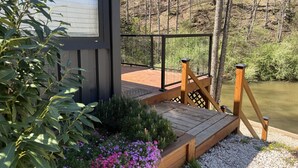 A wooden deck with a railing, surrounded by greenery and flowers. - The Hideaway on Tacketts Shipping Container (Hurricane)