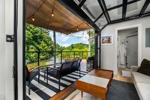 A modern interior with a balcony overlooking a lake, furnished with a sofa and a table. - The Hideaway on Tacketts Shipping Container (Hurricane)