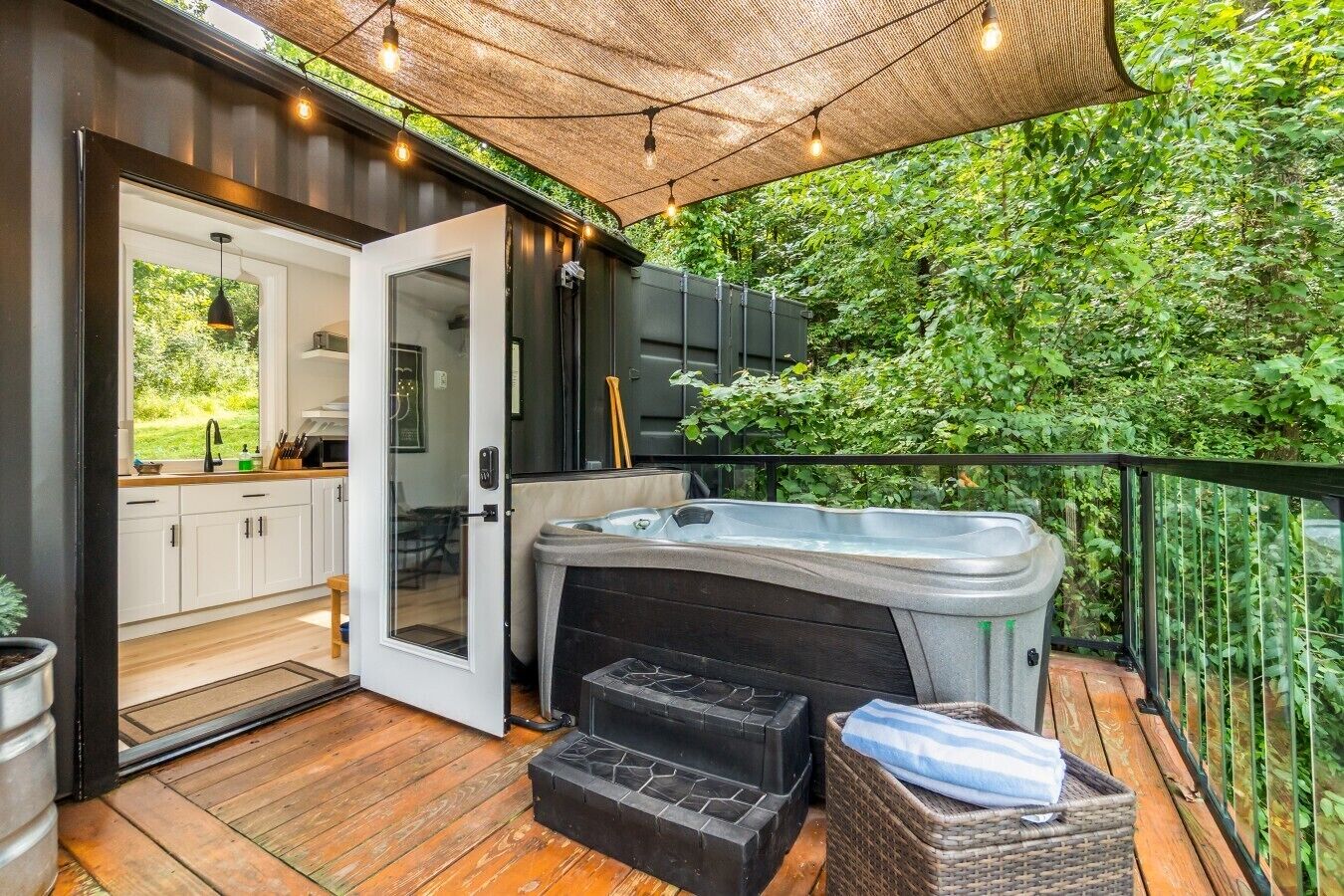 A deck with a hot tub, a wooden floor, and a view of greenery.
