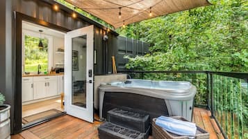 A deck with a hot tub, a wooden floor, and a view of greenery.