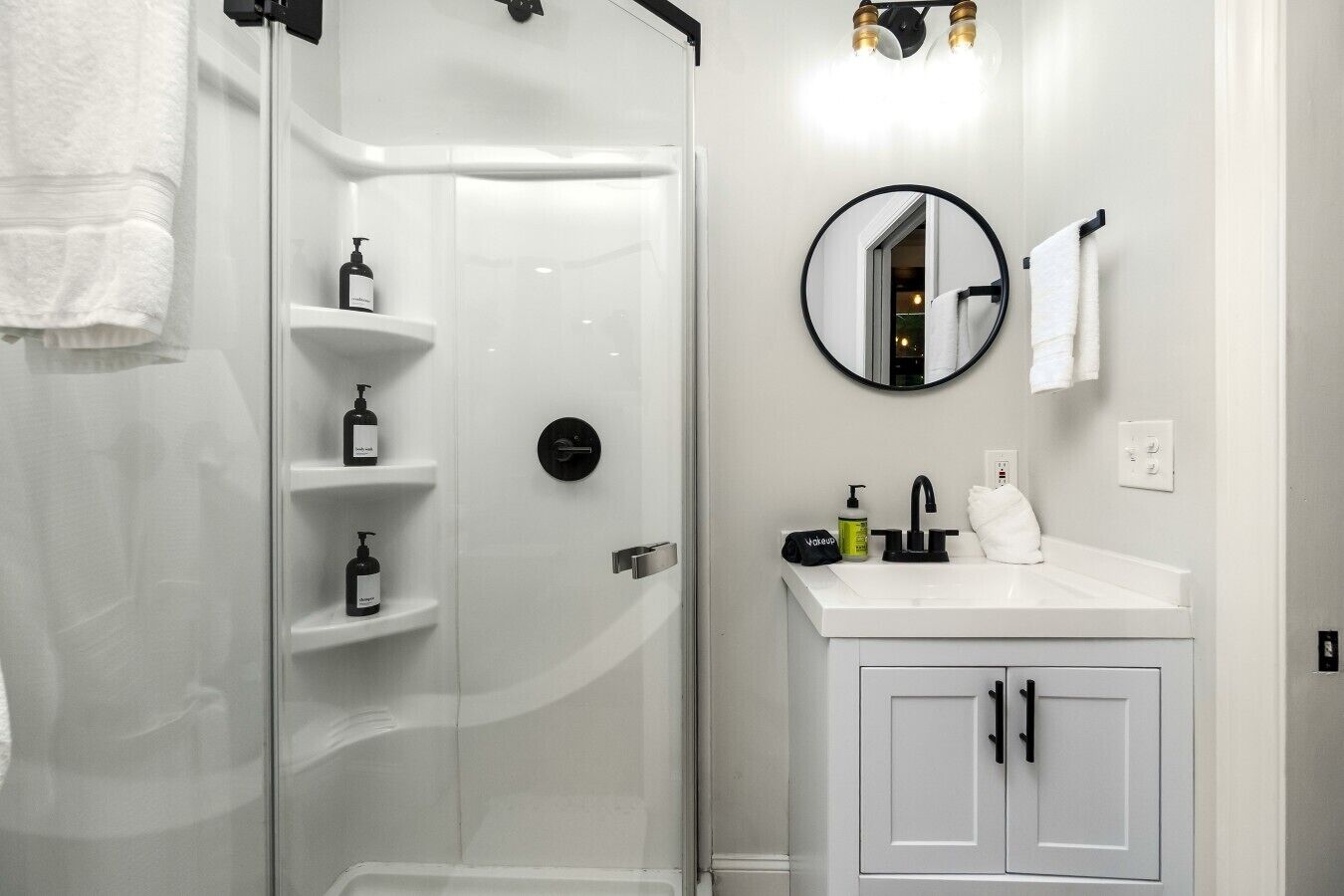A bathroom with a glass-enclosed shower, white vanity with a mirror, and a white towel hanging on the wall.