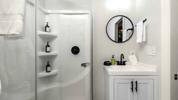 A bathroom with a glass-enclosed shower, white vanity with a mirror, and a white towel hanging on the wall.