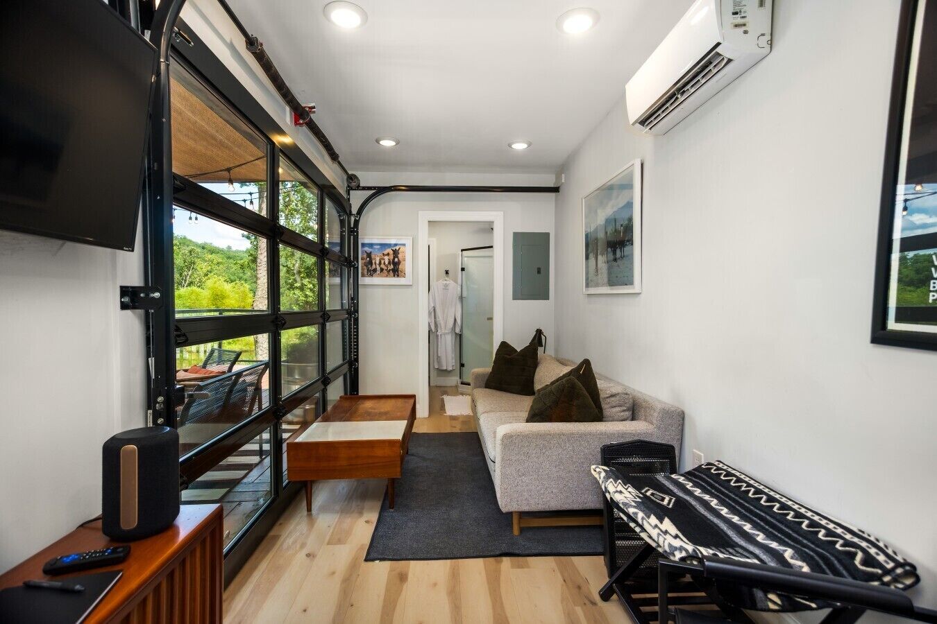 Ein modernes Interieur mit einer Couch, einem Couchtisch, einem Fernseher und einem Fenster mit Blick auf Grünflächen.