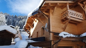 Een houten chalet met een balkon, omringd door met sneeuw bedekte bomen en een heldere lucht.