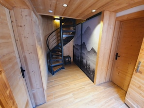 Un intérieur en bois avec un escalier en colimaçon, des murs en bois et une porte ornée d’une fresque représentant une montagne.