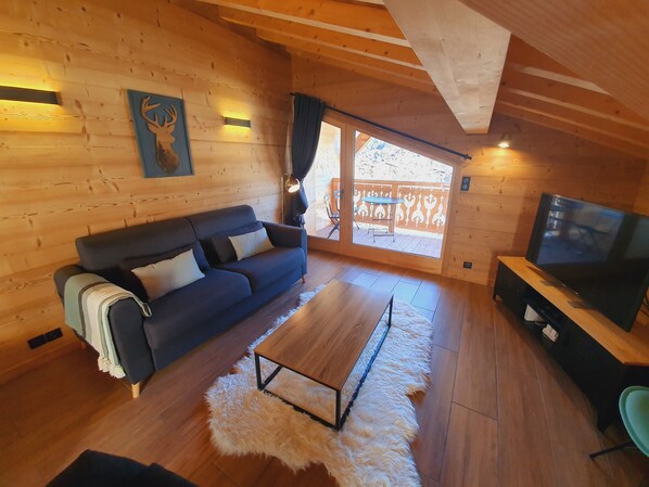 A cozy cabin interior with a wooden floor, a sofa, a TV, and a large window.