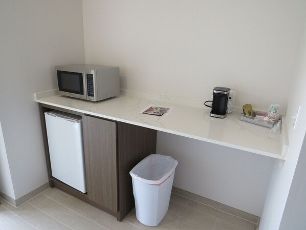 A compact kitchenette with a microwave, coffee maker, and a trash bin.