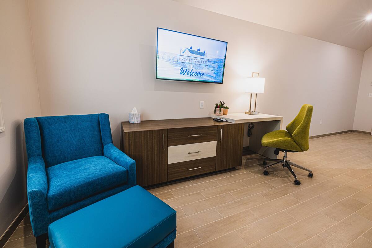 A room with a blue sofa, a green office chair, a desk with a lamp, and a television displaying "Frosty Valley Welcome".