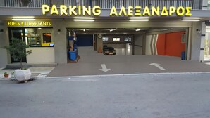 Entrada a un estacionamiento con flechas direccionales en el suelo, una gasolinera a la izquierda y un cartel que dice 'PARKING ALEXANAPOΣ'.