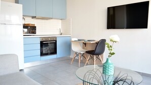 Una cocina moderna con armarios azules, horno empotrado y comedor con mesa y sillas de vidrio.