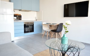 Una cocina moderna con armarios azules, horno empotrado y comedor con mesa y sillas de vidrio.