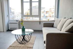 Un salón con una mesa de vidrio, un sofá color beige y vistas de edificios a través de un ventanal amplio.