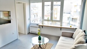 Un salón moderno con una mesa de centro de vidrio, un sofá y vistas de un paisaje urbano a través de grandes ventanales.